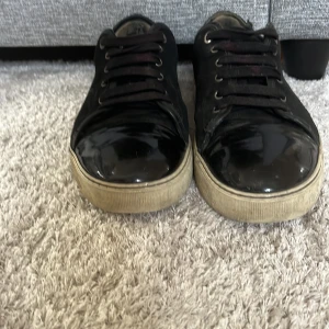 Svarta sneakers med lackdetaljer - Svarta sneakers med glansiga lackdetaljer på tån och klassisk snörning. Sulan är beige och ger en snygg kontrast till det svarta. Perfekta för dig som gillar en stilren men ändå unik look.