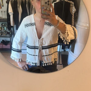 Blus/kofta - Säljer en vit boho-inspirerad blus med svarta broderade detaljer och knyt framtill. Jättefin nu på sommaren eller utomlands! Har använt fåtal gånger! Passar både XS och S!