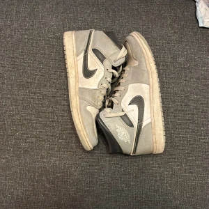 Nike Air Jordan 1 High Grå/Svart EUR 44 - Snygga Nike Air Jordan 1 High sneakers i grått och svart med klassisk Jordan-logga på sidan. Skorna har snörning, hög siluett och är tillverkade i skinn och syntet. Perfekta för dig som gillar streetstyle och vill sticka ut med en ikonisk modell.