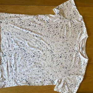 Superbra kvalitet Vit mönstrig t-shirt från Marine - Vit superbra kvalitet t-shirt från Marine med små  mönster i mörkblått och beige. Klassisk rund halsringning och korta ärmar. Tillverkad i mjuk bomull som känns skön mot huden. Perfekt för dig som gillar en clean men ändå lekfull stil.