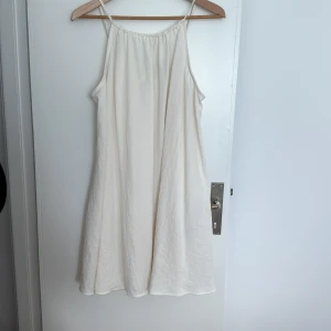 Vit a-linjeformad klänning från HM Divided - Vit a-linjeformad kort klänning med smala axelband och avslappnad passform. Klänningen har en enkel knytning bak och mycket vidd i kjolen. 