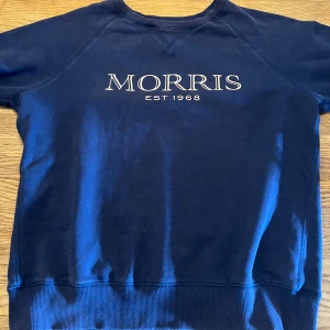 Mörkblå sweatshirt från Morris - Snygg mörkblå sweatshirt från Morris med vit broderad logga och texten 'EST 1968' på bröstet. Tröjan har rund halsringning, långa ärmar och ribbade muddar vid ärmslut och nederkant. Perfekt för en chill och stilren look.