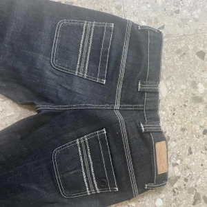 Mörkblå jeans från Lacoste - Snygga mörkblå jeans från Lacoste med vita sömmar. Midjemått: 37cm rakt över, Innerbenslängd: 79cm, Grenmått: 20cm🫶