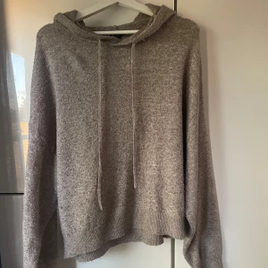 Beige stickad hoodie med huva - Mysig beige stickad hoodie med huva och snörning. Tröjan har långärmad design och ribbade muddar vid ärmslut och nederkant. Perfekt för dig som gillar en chill och avslappnad stil.