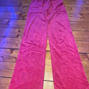 Juicy Couture rosa  - Rosa velourbyxor från Juicy Couture med breda ben och normal passform. Byxorna har snörning i midjan, två stora fickor bak med knappar och broderad JC-logga framtill. Använda ett par fåtal gånger.