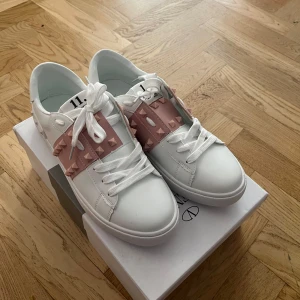 Valentino Rockstud sneakers vit/rosa - Jag har haft dem i 1 vecka dem va fel storlek jag kunde inte skicka tillbaka så jag säljer dem jag köpte dem för 7500kr och jag säljer för 2899 skit bra pris Snygga vita Valentino Rockstud sneakers med rosa band och ikoniska nitar. Skorna har rund tå, platt sula och vita snören. Tillverkade i skinn med coola detaljer som ger en lyxig och trendig vibe. Perfekta för dig som vill sticka ut med stil.