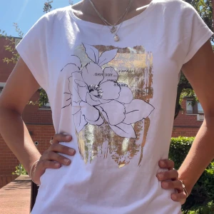 Vit t-shirt med blommigt tryck och guld - Jättefin t shirt med guld tryck från Reserved! Den är i storlek M men sitter jättefint på en som har S också! Den är helt ny med lappen kvar! Vid frågor eller funderingar så är det bara att höra av sig 💕