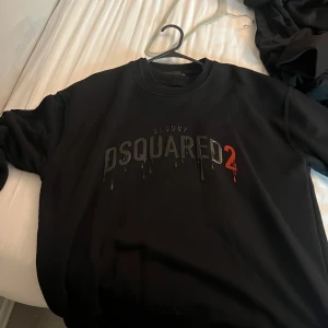 Svart sweatshirt från Dsquared2 - Svart sweatshirt från Dsquared2 med tryckt text 'BLOODY DSQUARED2' på bröstet. Snygg detalj med droppande effekt på bokstäverna och röd siffra 2. Tillverkad i 100% bomull och har rund hals samt långa ärmar.