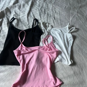 3-pack linne toppar i svart, vitt och rosa - Säljer tre stilrena linne toppar i svart, vitt och ljusrosa. Alla har smala axelband, där de alla har justerbara band för perfekt passform. Mjukt och stretchigt material som känns skönt mot huden. Perfekta att matcha med jeans eller kjol för en enkel och snygg look. Är kort så de visar magen🩷50kr för alla 3 eller 20kr st