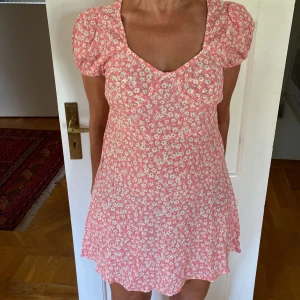 Rosa blommig kortklänning med puffärm - Supersöt rosa kortklänning med vita blommor och puffärmar. Klänningen har knytband i ryggen för snygg passform och är gjord i ett lätt, luftigt material. Perfekt för varma sommardagar. Är storlek Xs men passformen är som en S ☀️💕