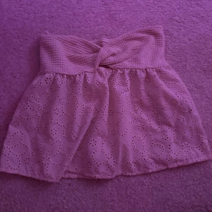 Beige bandeau tubtopp med spetsdetaljer - Supersöt beige bandeau tubtopp med twistad överdel och broderade blommor i spets. Perfekt för varma dagar och ger en romantisk vibe. Toppen är ärmlös och har en luftig känsla tack vare det broderade tyget.