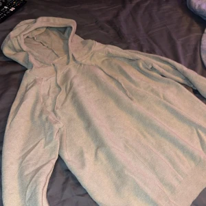 Beige stickad hoodie med snörning - Mysig beige stickad hoodie med huva och snörning. Tröjan har långa ärmar och en relaxed passform, perfekt för chill dagar. Enkel och stilren design som funkar till det mesta. Snyggt ribbade kanter vid huva och ärmslut.