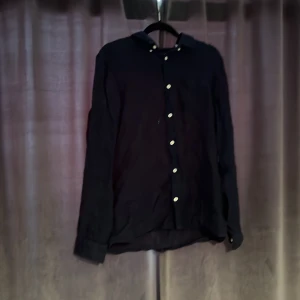 Mörkblå linneskjorta från GANT - Snygg mörkblå skjorta från GANT i 100% linne. Klassisk modell med krage, långa ärmar och vita knappar framtill samt vid ärmslut. Broderad GANT-logga på bröstfickan. Perfekt för sommaren och skön att ha över en klassisk tröja. Nypris: Ca 600kr