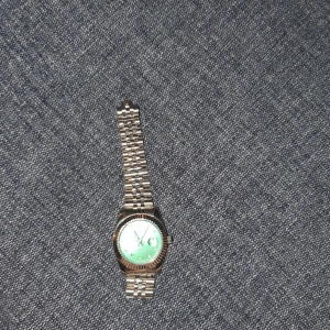 Silverfärgad klocka med grön urtavla - Stilren klocka i silverfärgat metallarmband och en grön urtavla med tydliga markeringar. Klassisk rund form och länkarmband som ger en tidlös look. Perfekt accessoar för dig som vill sticka ut med en färgglad detalj på handleden.