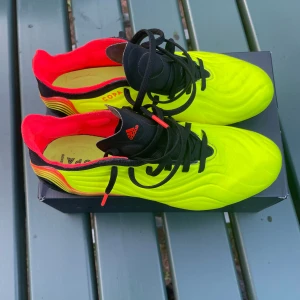 Adidas Copa Sense elite fg 40 - Snygga Adidas Copa Sense fotbollsskor i neon-gult med svarta och röda detaljer. Skorna har svart snörning, svarta dobbar och vågigt mönster på ovandelen. Insidan är röd och hälen har coola färgövergångar. Perfekta för dig som vill sticka ut på planen. De är använda 3 gånger men ser nästan helt nya ut. Adidas copa sense elite fg i storlek 40