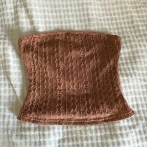 Brun stickad tubtopp från Shein  - Säljer en brun stickad tubtopp från Shein i storlek XS. Toppen har ett snyggt kabelstickat mönster och är axelbandslös, perfekt för att skapa en chill och trendig look. Materialet är mjukt och stretchigt, vilket gör den bekväm att bära hela dagen.