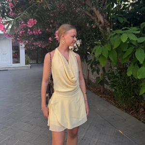 Ljusgul omlottklänning med öppen rygg - Supersöt ljusgul kortklänning med omlott-drapering framtill och snygg öppen rygg med knyt i nacken. Klänningen är ärmlös och har ett flowigt, lätt tyg som ger en fräsch sommarkänsla.💛💛