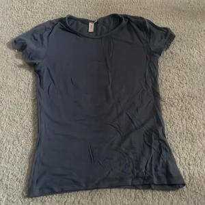 Mörkblå basic t-shirt från Nelly - En enkel och stilren mörkblå t-shirt från Nelly i storlek XS. T-shirten har rund halsringning och korta ärmar, perfekt för en clean och avslappnad look. Materialet känns mjukt och följsamt mot huden.