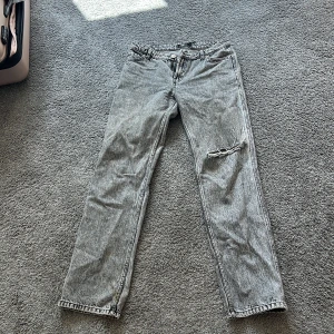 Grå straight jeans från FB Sister - Säljer ett par grå jeans från FB Sister i straight fit med slitning på ena knät. Jeansen har klassisk femficksdesign, bälteshällor och dragkedjegylf. Perfekta för dig som gillar en avslappnad och trendig look.