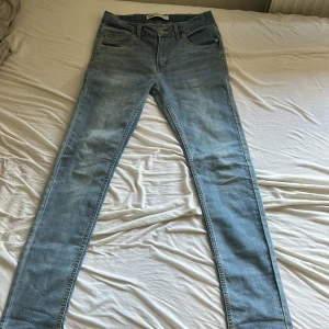 Levi's 510 ljusblå skinny jeans - Säljer ett par Levi's 510 skinny jeans i ljusblå tvätt. Klassisk femficksmodell med dragkedja och knapp, samt Levi's ikoniska läderpatch bak. Jeansen har smal passform och är tillverkade i mjukt bomullsjeansmaterial. Levis logan för bak är lite sönder och lite där fram som man ser på bilderna. Storlek 176cm 16A nypris 600kr