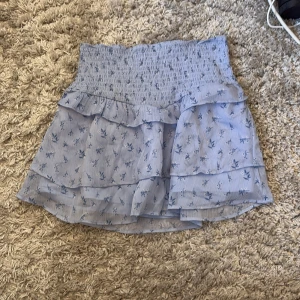 Blå blommig volangkjol - Supersöt ljusblå kortkjol med blommigt mönster och flera volanger. 