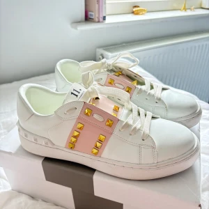 Valentino Rockstud sneakers i vitt och rosa - Säljer ett par jätte söta Valentino Rockstud sneakers i vitt skinn med ljusrosa paneler och guldiga nitar. Skorna har snörning, platt sula och rund tå. Dom är bara använda ett fåtal gånger eftersom dom är för små för mig, så tyvärr måste jag sälja dom 💓
