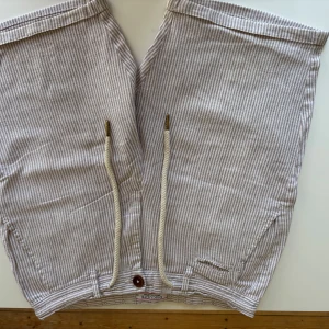 Randiga shorts i linne och bomull från italienska Disculpe. Storlek 44/ XS - Snygga brun- och vit randiga shorts i linne och bomull från italienska Disculpe Basic Collection. De har snörning i midjan, bruna knappar och praktiska fickor både fram och bak. Storlek 44/ XS