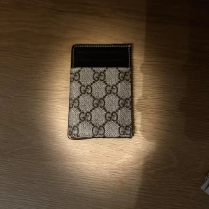  korthållare i monogram canvas - Snygg korthållare fmonogram. Framsidan är beige med bruna loggor och baksidan är svart med plats för flera kort. Slimmad design i canvas och skinn, perfekt för dig som vill ha stilren accessoar i fickan.