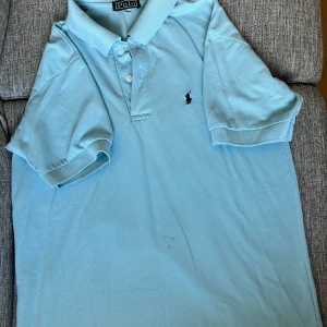 Ralph Lauren piké  - Klassisk piké från Ralph Lauren – stilren, tidlös och alltid rätt. Tillverkad i mjuk bomull med den ikoniska broderade ponnyn på bröstet. Perfekt för både vardag, jobb eller mer uppklädda tillfällen. En mångsidig favorit i garderoben som aldrig går ur stil.