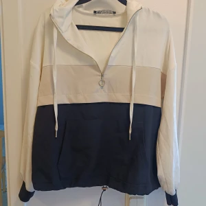 Vit och marinblå hoodie med half zip - Snygg hoodie från A&I i färgblockad design med vit, beige och marinblå. Half zip framtill, huva med snören och stor magficka. Perfekt för chill dagar och streetstyle. Långärmad och loose passform för extra komfort.