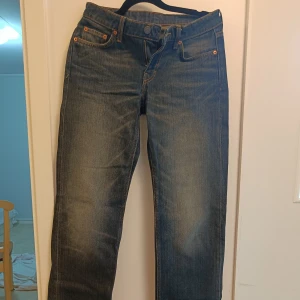 Levi's 501 blå jeans straight fit - Klassiska blå Levi's 501 jeans med rak passform och snyggt slitna detaljer. Jeansen har fem fickor, orangea sömmar och knappgylf. Perfekta för dig som gillar en tidlös och avslappnad stil.