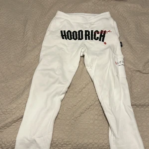 Vita mjukisbyxor från Hoodrich S - Snygga vita mjukisbyxor från Hoodrich i storlek S. Byxorna har svart och röd broderad logga framtill och tryck på benet. De har en avslappnad passform, elastisk midja och praktisk ficka på sidan. Perfekta för en chill och street-inspirerad look. Pris kan diskuteras.