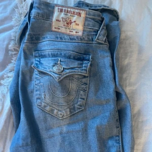 True Religion ljusblå bootcut jeans - Säljer ett par ljusblå jeans från True Religion, modell Becca Mid Rise Bootcut. Jeansen har klassiska kontrastsömmar, snygga detaljer på bakfickorna och silverfärgade knappar. Perfekt för dig som gillar en avslappnad men ändå trendig look.
