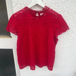Röd rosa spetsblus från Holly & Whyte - Säljer en röd blus i spets från Holly & Whyte by Lindex. Blusen har korta ärmar, med fina guldknappar i nacken.  (Måste säga att den är mycket mer rosa i verkligheten än på bilden) 