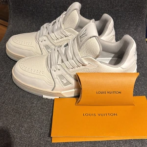 Louis Vuitton vita sneakers #54 - Exklusiva Louis Vuitton sneakers i helvitt skinn med präglad LV-logga på plösen och #54 broderat på hälen. Snygg chunky sula, rund tå och klassisk snörning. Lyxig känsla med detaljer i premiumläder och diskreta grå accenter. Perfekta för dig som vill sticka ut med stil. ✅                         Storlek 45, box rinns tyvärr inte men kvitto samt oficiellt LV kort medkommer. Skriv vid intresse!