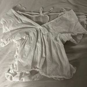 Vit topp med volangärm - Supersöt vit omlottopp med v-ringning och knyt i ryggen. Toppen är i stretchigt mjukt svalt material