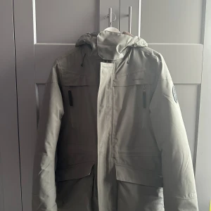 Grå parkajacka från Winter trails storlek  M - Oanvänd. Skickar iväg samma dag eller dagen efter🙌🏼Säljer en parkajacka från Winter Trails i storlek M. Jackan har huva, flera fickor med dragkedja och coolt snöflinge-märke på ärmen. Insidan är quiltad i senapsgult och materialet är slitstarkt polyester. Perfekt för kalla vinterdagar och outdoor vibes.