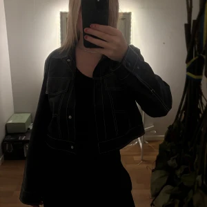 Svart croppad skinnjacka med kontrastsömmar - Säljer en svart croppad skinnjacka med vita kontrastsömmar från Bershka. Storlek xs men passar även s