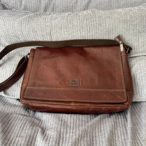 Brun axelväska i läder från BaooBaoo - Snygg brun axelväska från BaooBaoo i äkta läder med justerbar axelrem i tyg. Väskan har flera fack, dragkedja med metall-detaljer och stilrena sömmar. Perfekt för dig som vill ha en klassisk och praktisk väska med tidlös look.