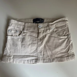 Beige lågmidjad minikjol  - Supersnygg beige kort jeanskjol från Bershka med klassisk femficksdesign, bälteshällor och knappstängning fram. Kjolen har raka linjer och är tillverkad i mjuk bomull med en lätt stretchig känsla. Perfekt för dig som gillar en clean och enkel look. Köpt på en spansk marknad❤️