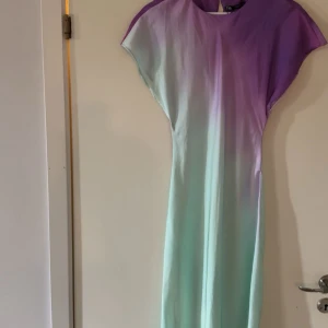 Långklänning i lila och mintgrön - Supersnygg långklänning från zara med mjuk övergång från lila upptill till mintgrönt nedtill. Klänningen har korta ärmar och ett flowigt, rakt fall. Perfekt för dig som gillar färg och vill sticka ut med en unik gradient-effekt. Nypris 549