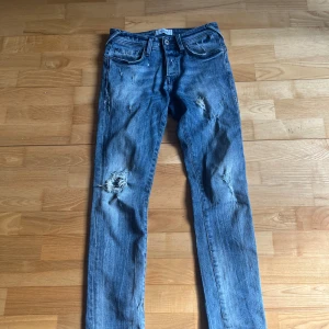 Blå jeans från Jack & Jones - Säljer ett par blå jeans från Jack & Jones med snygga slitningar 