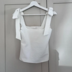 Vit linnetopp från Zara - Supersnygg vit linnetopp från Zara med breda axelband som knyts i stora rosetter på axlarna. Toppen har rak, något croppad passform och är tillverkad i ett mjukt, lite stretchigt material. Perfekt för en fräsch och stilren look.