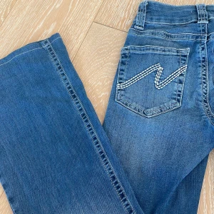 Blå bootcut jeans från Nelly - Snygga blå jeans från Nelly med bootcut passform och låg midja. Storlek 32 och är uppsydda, inre mått på benen 72cm 