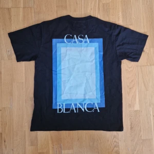 Svart Casablanca t-shirt med blå print - Helt ny svart t-shirt från Casablanca med stort grafiskt tryck i blå toner och texten 'Casa Blanca' på ryggen samt mindre print på bröstet. Klassisk rund hals och korta ärmar. Perfekt för dig som gillar stilrena men ändå unika plagg. Storlek står S men passar M !