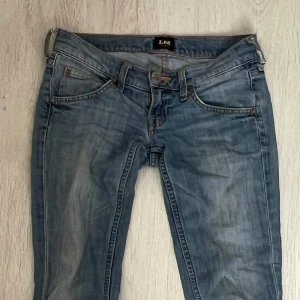 Lågmidjade jeans - Säljer ett par ljusblå väldigt lågmidjade jeans från Lee. Jeansen har klassisk femficksdesign, bootcut passform och snygga slitningar. Tillverkade i bomull med dragkedja och knapp framtill. Perfekta till sneakers eller boots. Sydda bootcut själv men syns nästan inte! 