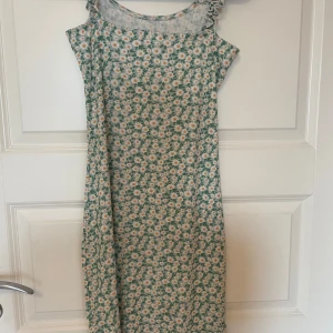 Blommig kort klänning med volangband - Supersöt klänning som slutar ovanför knäna med vitgult blommönster, Klänningen har ärmlös design och volangband vid axlarna som ger en gullig touch. Perfekt för sommarens alla tillfällen och riktigt skön att bära.