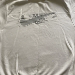 Vit Nike sweatshirt med Swoosh-tryck - Säljer en stilren vit sweatshirt från Nike med stort Swoosh-tryck och text på bröstet. Tröjan har rund halsringning, långa ärmar och är gjord i mjuk bomullsmix. Perfekt för dig som gillar clean streetstyle och sportiga vibes.