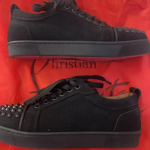 Christian Louboutin svarta sneakers med nitar - Svarta sneakers från Christian Louboutin i mocka med coola svarta nitar på tån och klassisk röd sula. Skorna har snörning och en chunky platt sula. Perfekta för dig som vill sticka ut med en edgy och lyxig vibe.