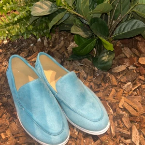 Ljusblå mockaloafers med vit sula - Snygga ljusblå loafers i mocka med vit platt sula och beige innersula. Skorna har en klassisk, stilren design med rund tå och passar perfekt till en avslappnad men ändå uppklädd look. Perfekta för dig som vill sticka ut med färg på fötterna.